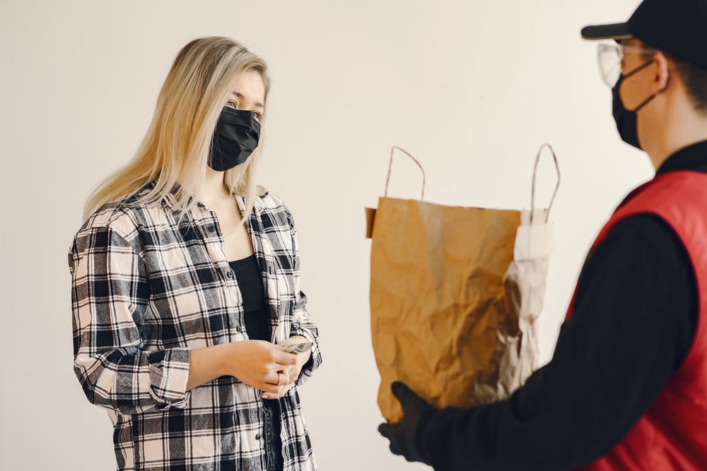 man giving woman grocery delivery with mask on